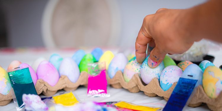 a person is putting colored eggs in a carton
