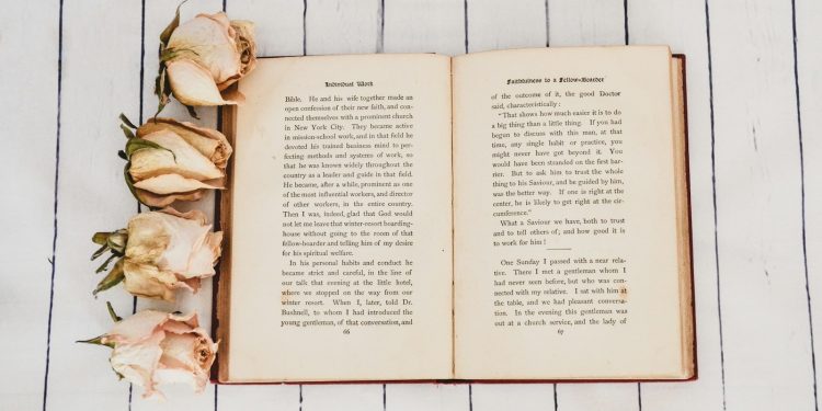 white book opened near four white roses