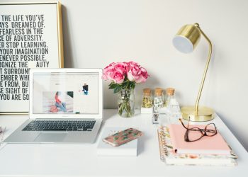MacBook Air beside gold-colored study lamp and spiral books