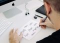 person writing on white printer paper in front of silver iMac