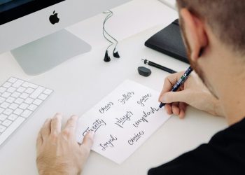 person writing on white printer paper in front of silver iMac