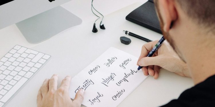person writing on white printer paper in front of silver iMac